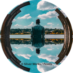 Person in Jeansjacke steht vor einem See, umgeben von einem Betonbogen, mit spiegelbildlicher Reflexion im Wasser.