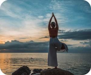 Frau von hinten macht Yoga vor einer See-Kulisse