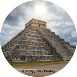 Steinstufenpyramide El Castillo in Chichén Itzá unter bewölktem Himmel, mit Sonnenlicht über der Spitze.