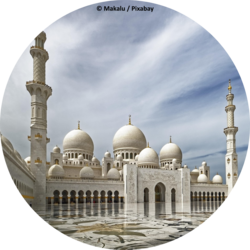 Weiße Moschee mit großen Kuppeln und schlanken Minaretten, davor ein weitläufiger, spiegelnder Innenhof mit floralen Mosaiken.