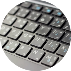 Nahaufnahme einer schwarzen Tastatur mit lateinischen und arabischen Buchstaben sowie blauen Ziffern und Symbolen.