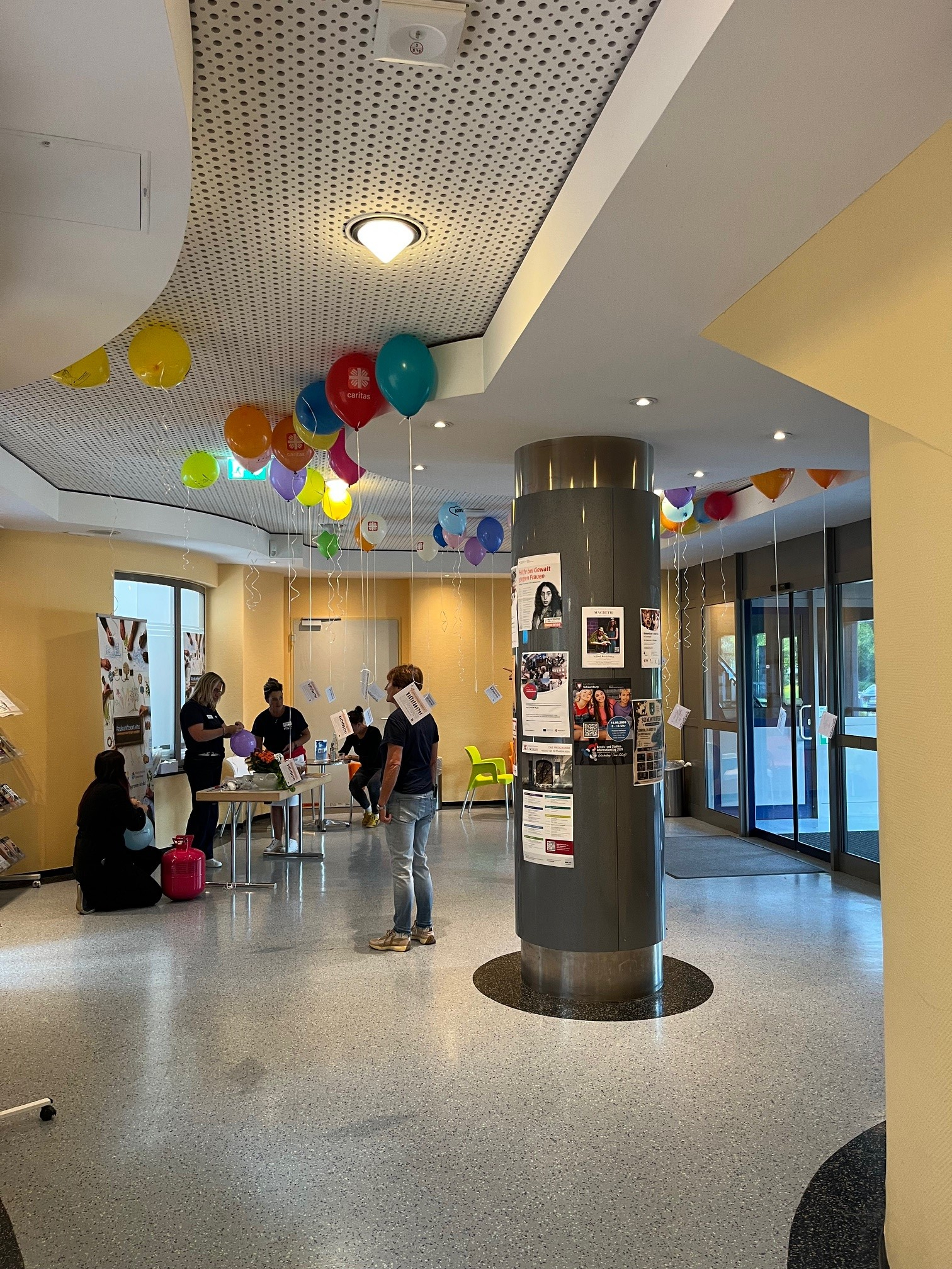 Im Foyer der VHS Schaumburg hängen zum Tag der Frauengesundheit zahlreiche bunte Luftballons. Mehrere Frauen bereiten Informationsstände und Angebote für die Veranstaltung vor.