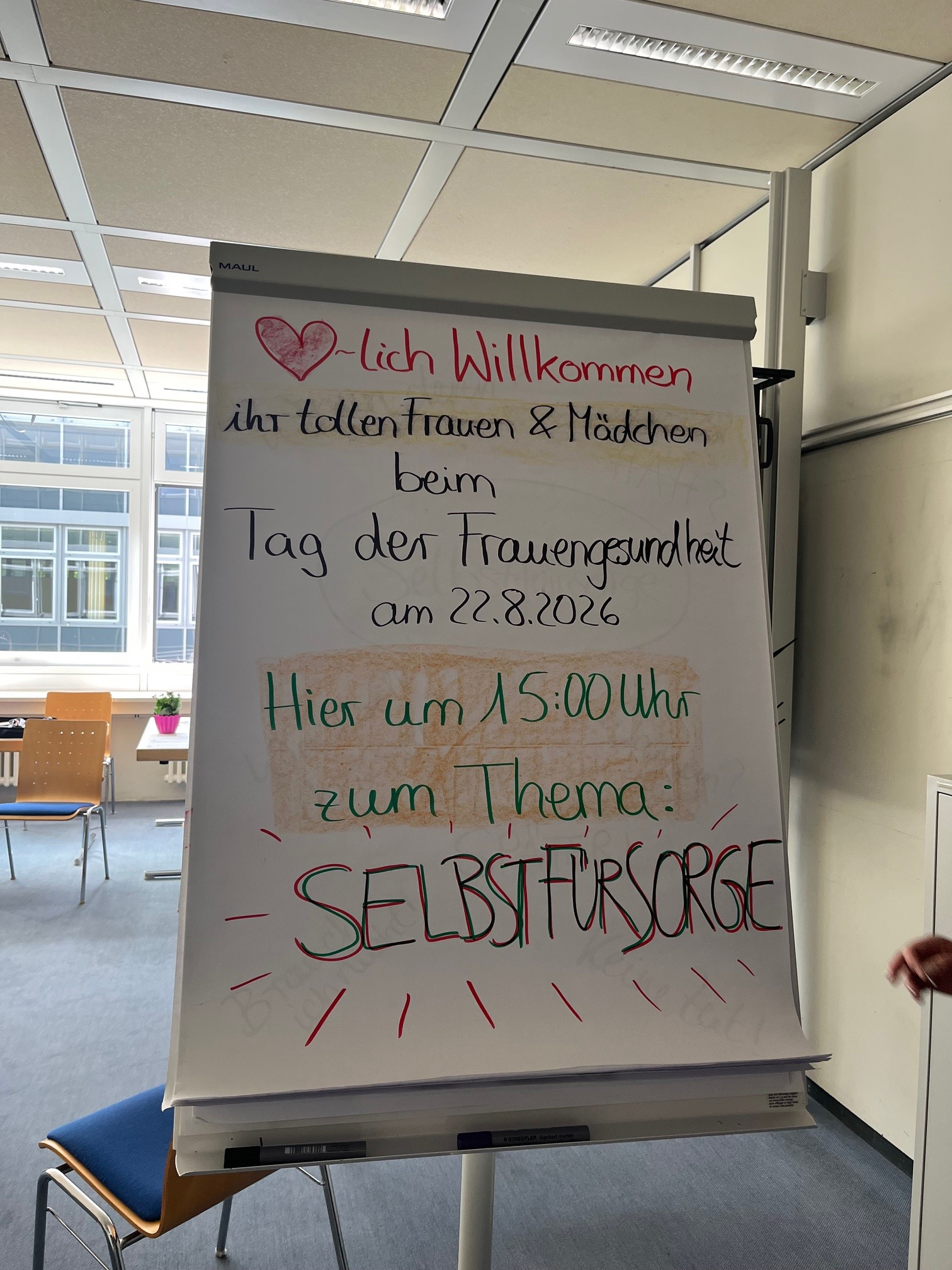Ein Flipchart begrüßt die Besucherinnen zum Tag der Frauengesundheit und kündigt ein Angebot zum Thema Selbstfürsorge an.