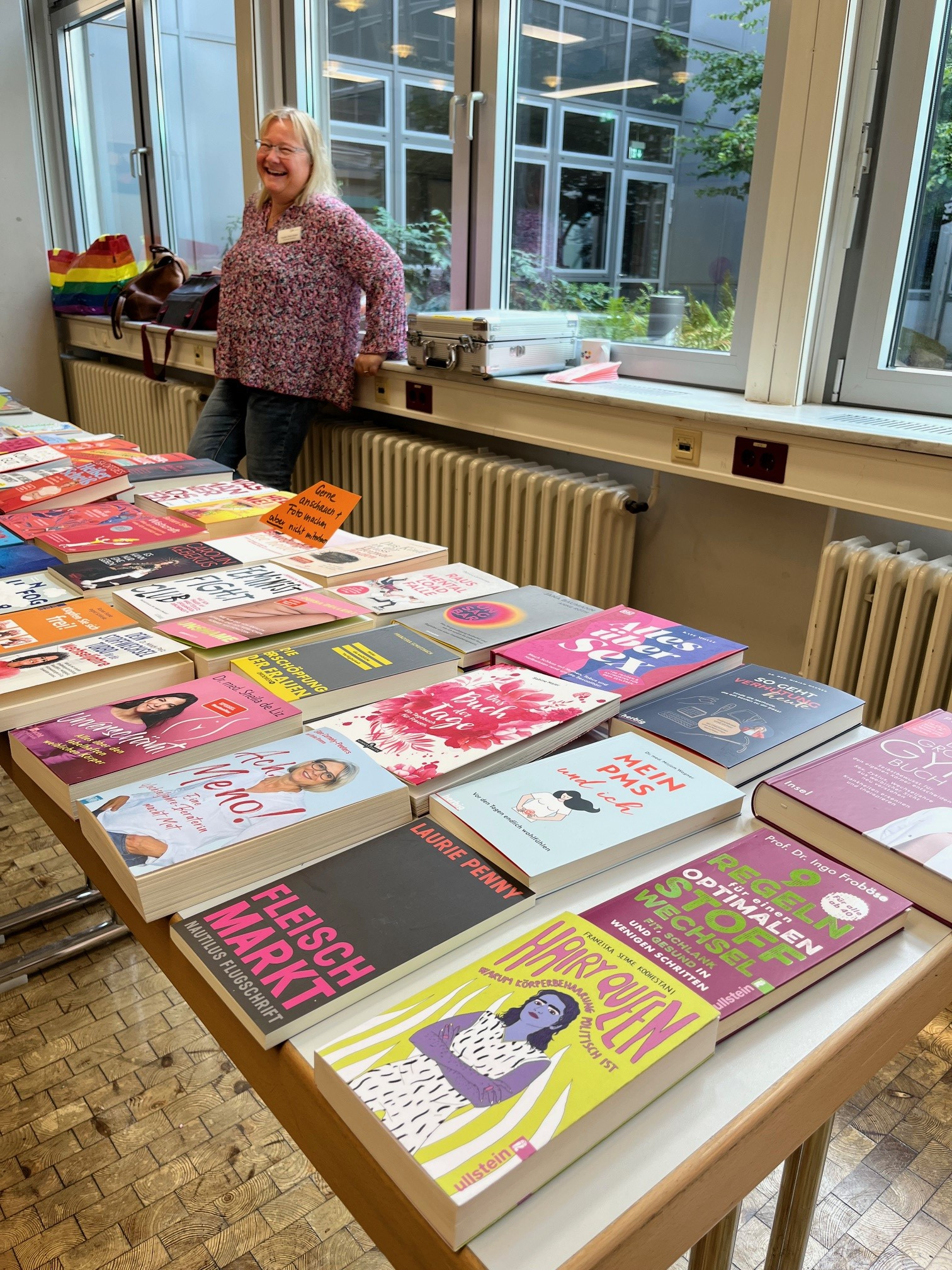 Eine Frau steht hinter einem Büchertisch mit zahlreichen Büchern zu Frauengesundheit, Sexualität, Wechseljahren und weiteren Frauenthemen.