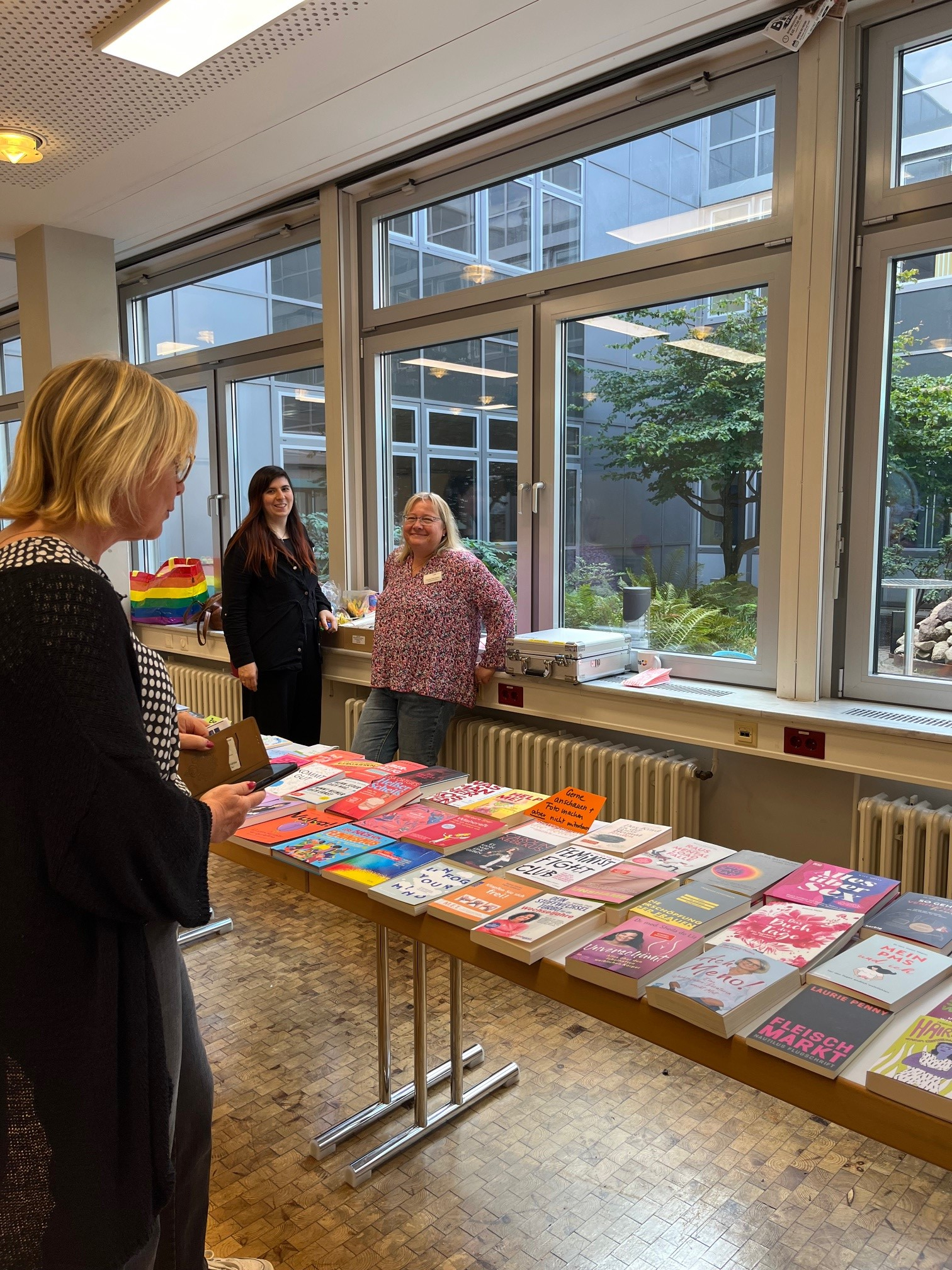 Mehrere Frauen stehen an einem Büchertisch mit Literatur zu Frauengesundheit und Frauenthemen und kommen miteinander ins Gespräch.